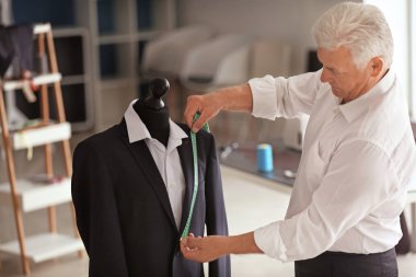 Mature tailor taking measurements of male jacket on mannequin in atelier clipart