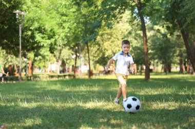 Küçük çocuk parkta futbol oynuyor.