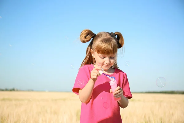 可爱的小女孩吹肥皂泡在田野上的阳光明媚的一天 — 图库照片