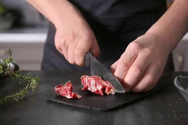 Man cutting raw meat on slate plate in kitchen
