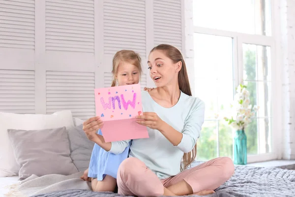 Mother receiving greeting card from her cute little daughter at home