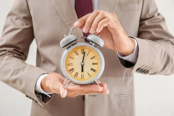 Businessman holding alarm clock on light background, closeup. Time management concept