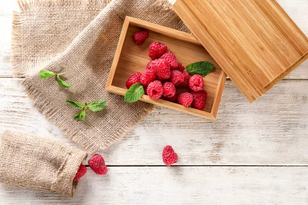 Wooden box with sweet ripe raspberries on table