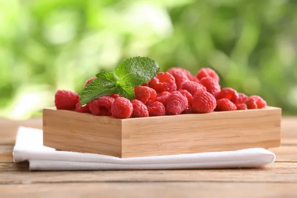 Wooden box with sweet ripe raspberries on table outdoors