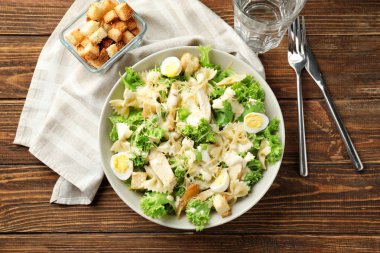 Ahşap masa üzerinde bir kapta makarna ile lezzetli Sezar salatası