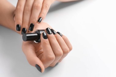 Beyaz arka planda, closeup vernik şişe tutan şık siyah manikür kadınla
