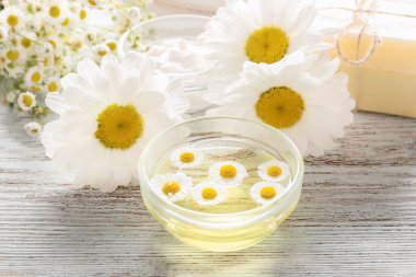 Esans ve ahşap masa üzerinde papatya çiçeği ile kase