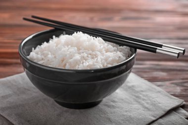 Haşlanmış beyaz pirinç ve ahşap masa üzerinde yemek çubukları ile kase