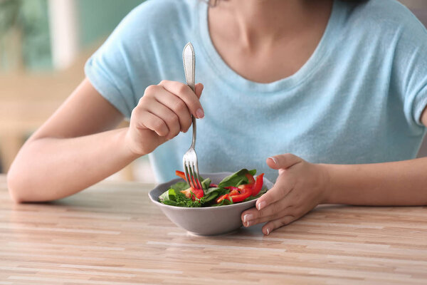 Young woman eating healthy salad with vegetables at home