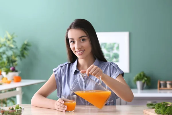 若い女性の台所でガラスに水差しから柑橘類のジュースを注いで — ストック写真