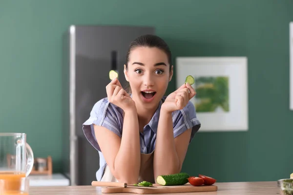台所でキュウリのスライスを持つ面白い若い女性 — ストック写真