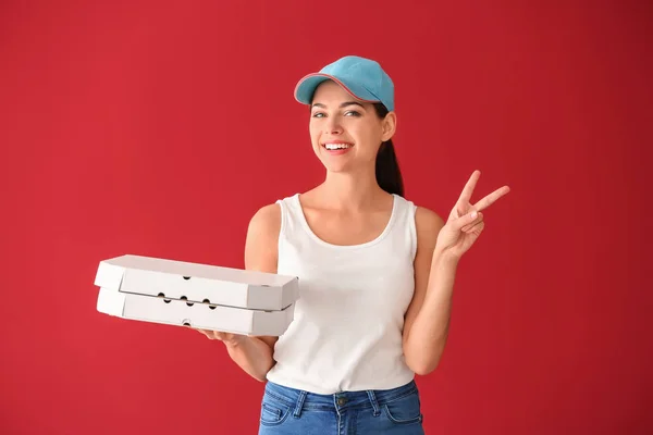 Young woman with pizza boxes showing victory sign on color background. Food delivery service