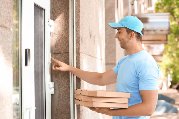 Young man with pizza boxes ringing doorbell outdoors. Food delivery service