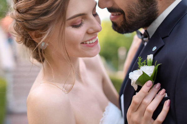Happy young bride attaching buttonhole to her groom's jacket
