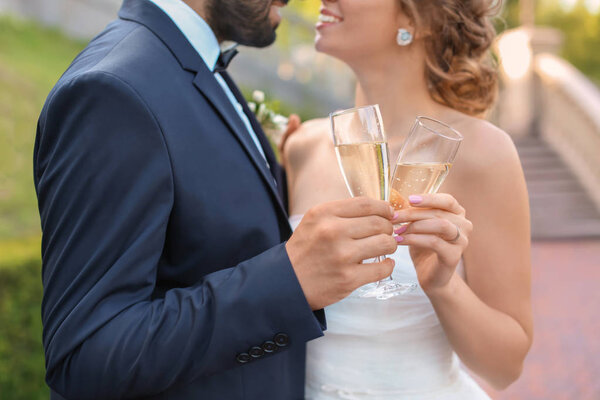Happy wedding couple with glasses of champagne outdoors