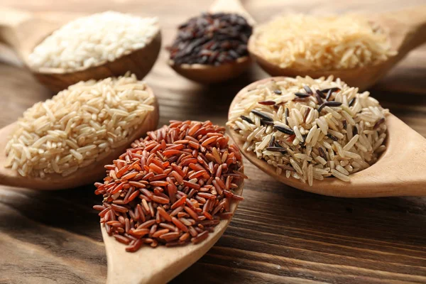 Different types of rice in spoons on wooden background