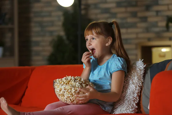 晚上在沙发上看电视的小女孩吃爆米花 — 图库照片