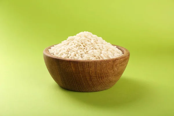 Wooden bowl with raw rice on color background