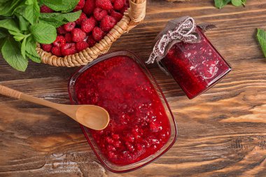 Ahşap masa üzerinde lezzetli frambuaz reçeli ile kase ve cam kavanoz