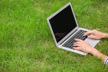 Park yeşil çimenlerin üzerinde dinlenme dizüstü bilgisayar ile genç kadın