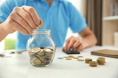 Paralar cam kavanozun içine masanın üzerine koyarak adam. Tasarruf kavramı