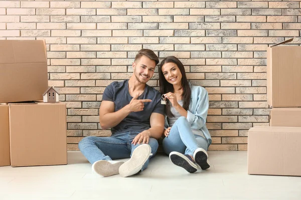Young happy couple with key and moving boxes sitting on floor at new home
