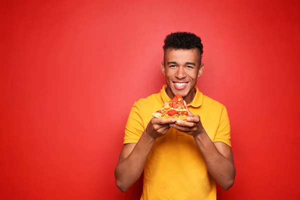 Young African American Man Eating Slice Delicious Pizza Color Background — Stock Photo, Image