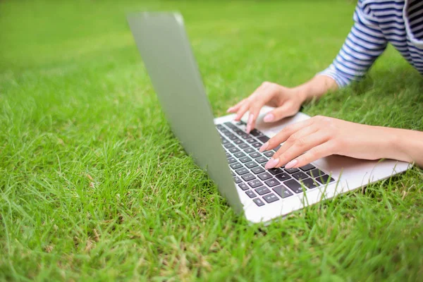 Young woman with laptop resting on green grass in park