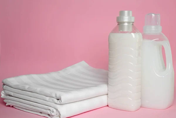 Stack of clean bed sheets and bottles with detergent on color background