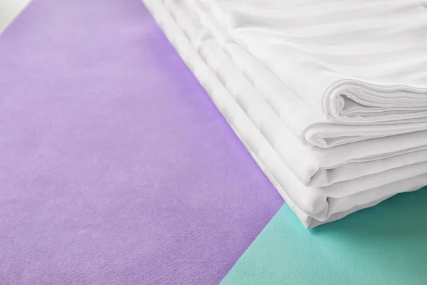 Stack of clean bed sheets on color background, closeup