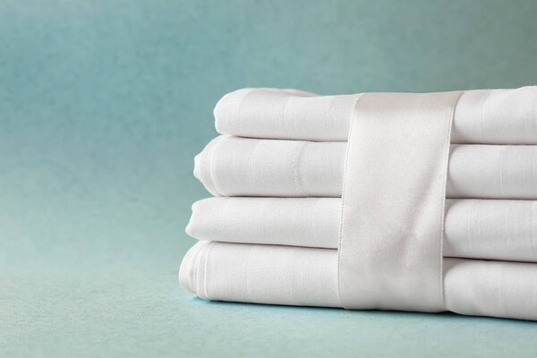 Stack of clean bed sheets on color background