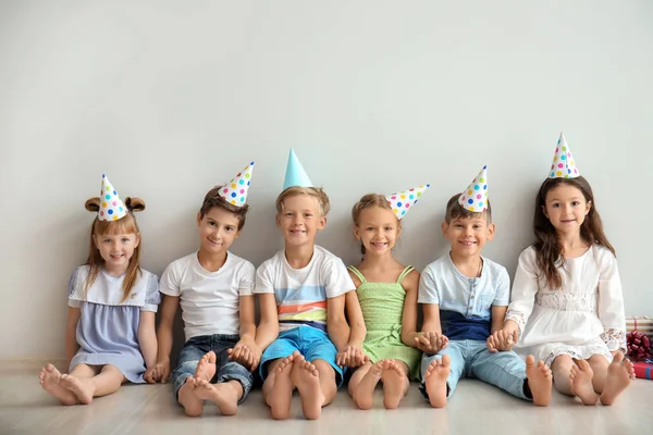 Lindos Niños Pequeños Sombreros Cumpleaños Sentados Suelo Cerca Pared Luz —  Fotos de Stock