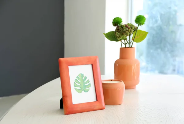 Frame with picture of green leaf and burning candle on white table