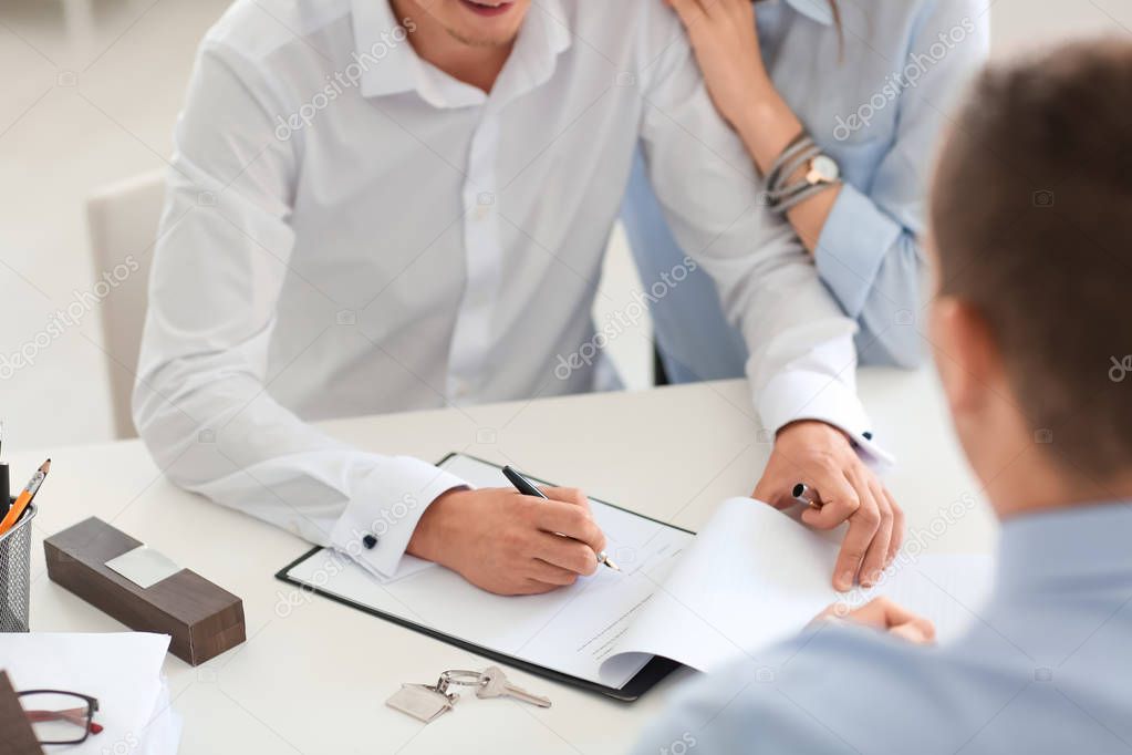 Young man signing a contract for buying house in office of real estate agent