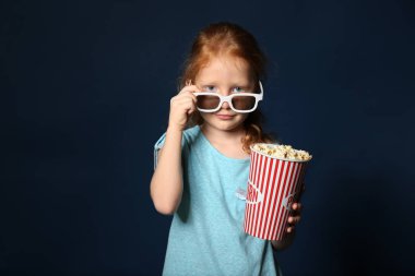 Sevimli küçük kız fincan koyu arka plan üzerinde 3d sinema gözlüklü patlamış mısır ile