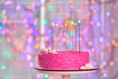 Lezzetli Doğum günü pastası ile stand ve bulanık ışıklar karşı mumlar yanan