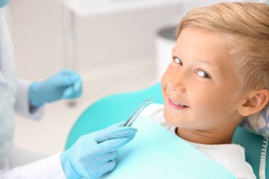 Dişçi klinikte küçük çocuğun dişlerini muayene ediyor.