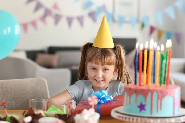 Cute little girl with birthday cake at table