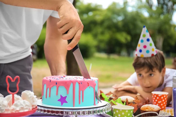 Father cutting tasty cake at birthday party outdoors