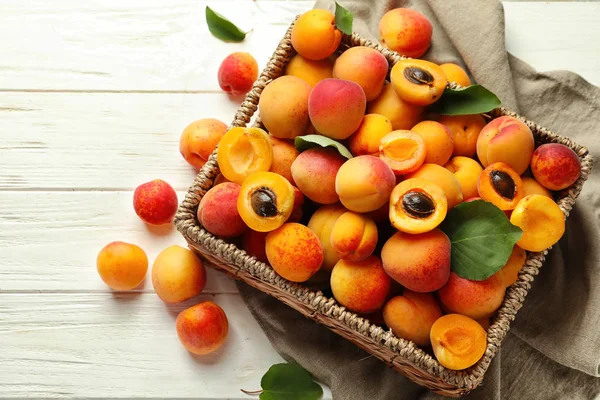 Wicker box with ripe sweet apricots on white wooden background