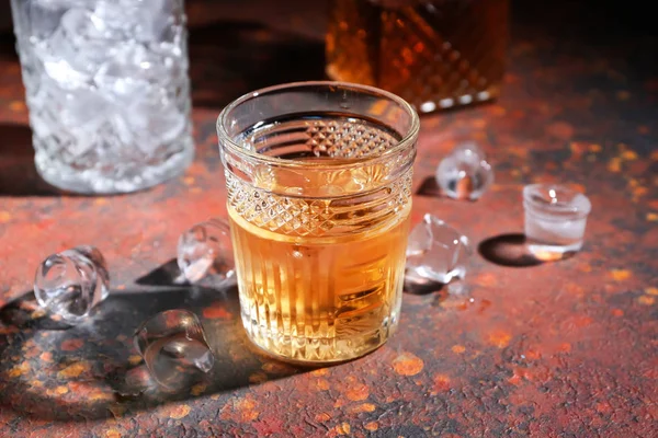 Glass of icy whiskey on color table