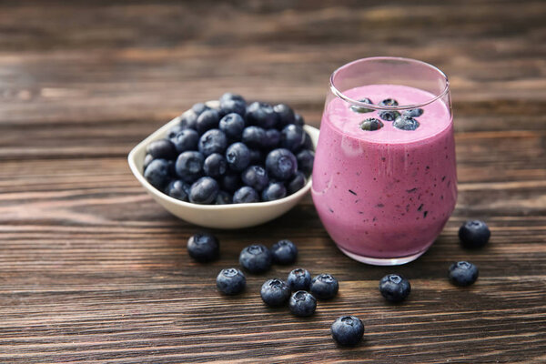 Glass of tasty blueberry smoothie and bowl with fresh berries on wooden table