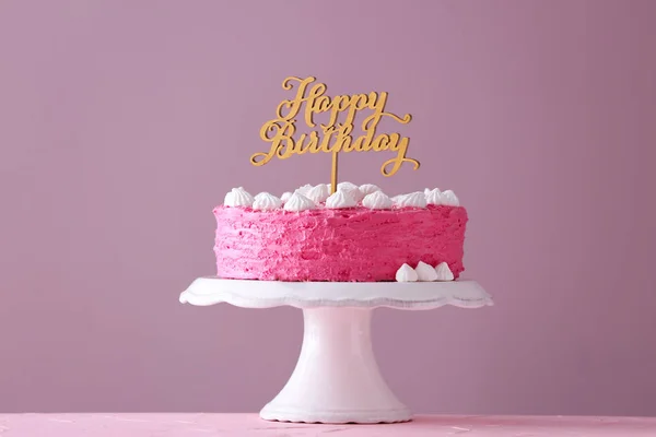 Stand with delicious birthday cake on table against color background