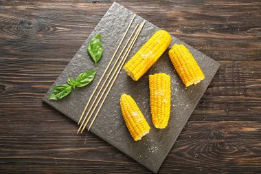 Ahşap masa üzerinde lezzetli mısır koçanı ile kayrak plaka