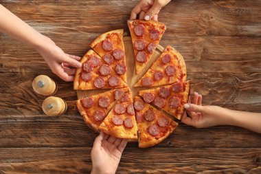 Dilim lezzetli pizza ahşap tablodan alan genç insanlar