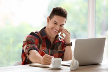 Kafede çalışırken cep telefonuyla konuşan genç serbest meslek