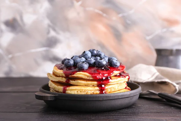 Frying pan with tasty pancakes, jam and blueberries on wooden table