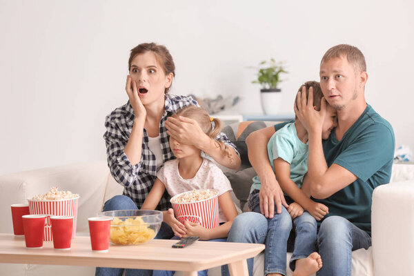 Family eating popcorn while watching scary movie at home