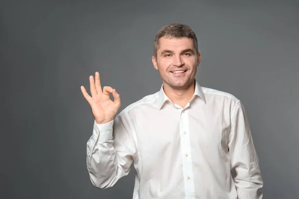 Schöner Geschäftsmann Zeigt Geste Auf Grauem Hintergrund — Stockfoto