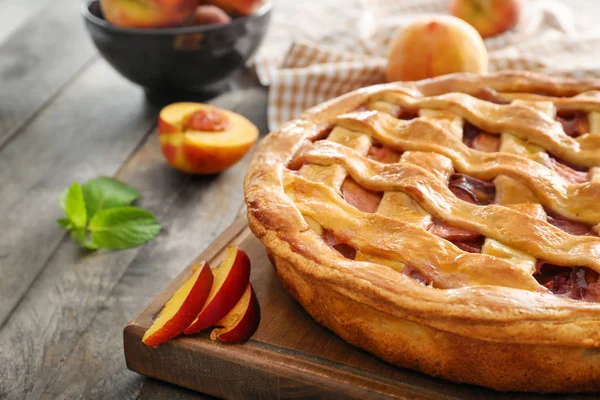 Board with delicious peach pie on wooden table, closeup